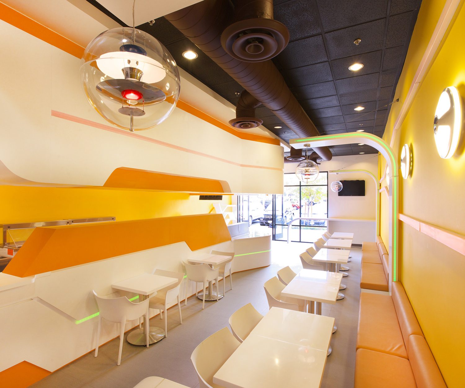 飲料店設計裝潢(側拍)：用餐區展示了符合品牌色的明亮橙黃牆壁、椅子配合桌子與吧檯的白，增強了活潑的潮流氛圍。