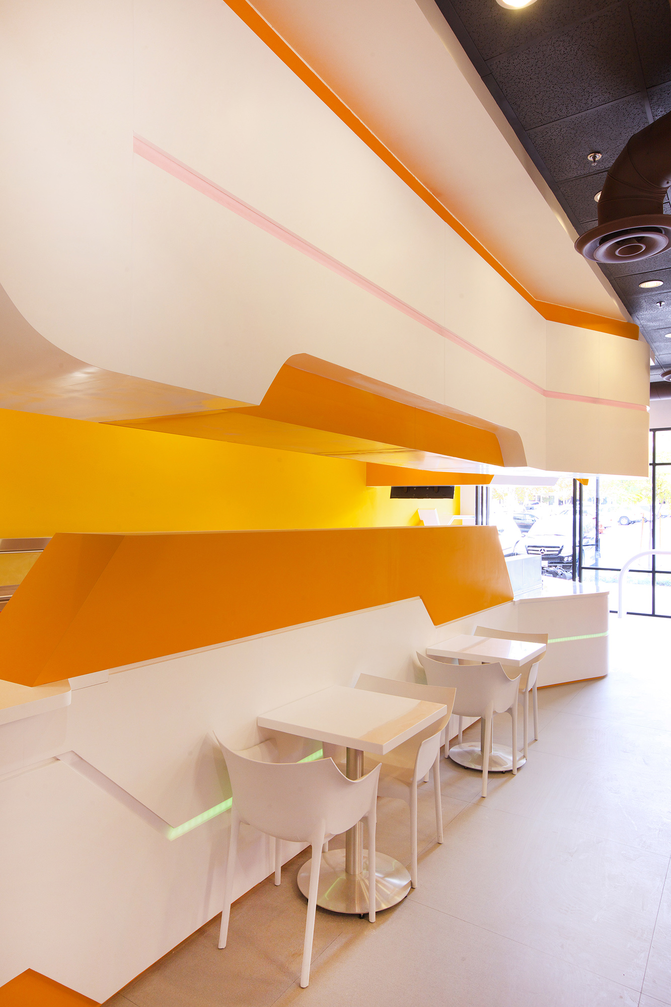 飲料店吧檯設計：以橙與白的品牌色，配合曲面、平面的變化，再輔以燈光營造年輕潮流感。